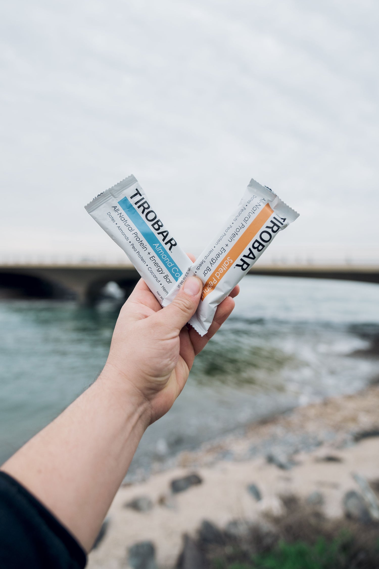 Enjoy Tirobar Protein Bars on the Go: A Pair of Tasty Bars with Scenic View of Water and Bridge in the Background