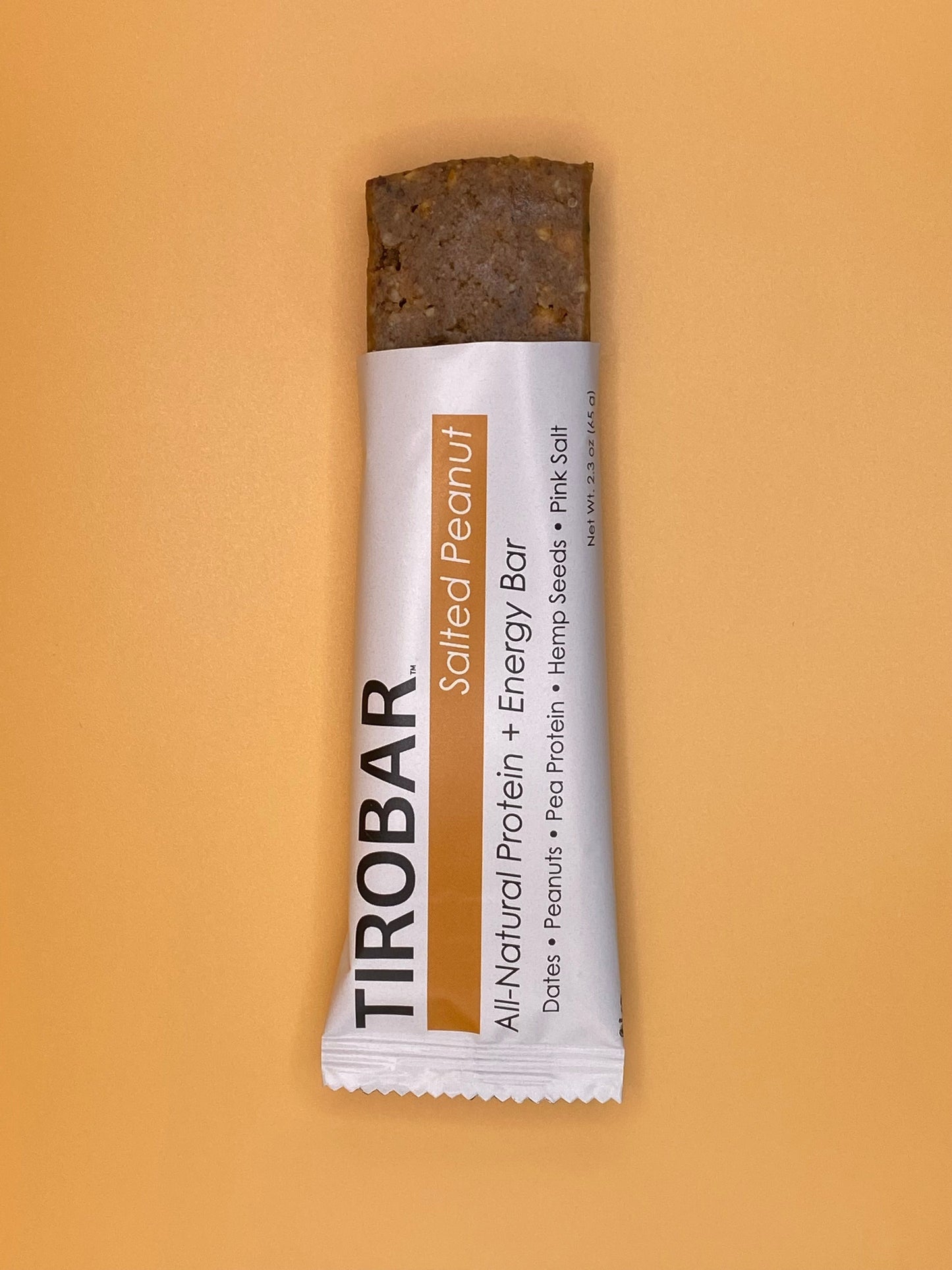 A salted peanut TIROBAR, a vegan and all natural protein bar, is shown half out the wrapper, showing peanuts and bar contents against an orange background. 